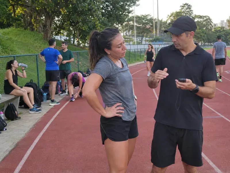 Corredora conversando com o treinador na pista durante o treino em grupo da assessoria