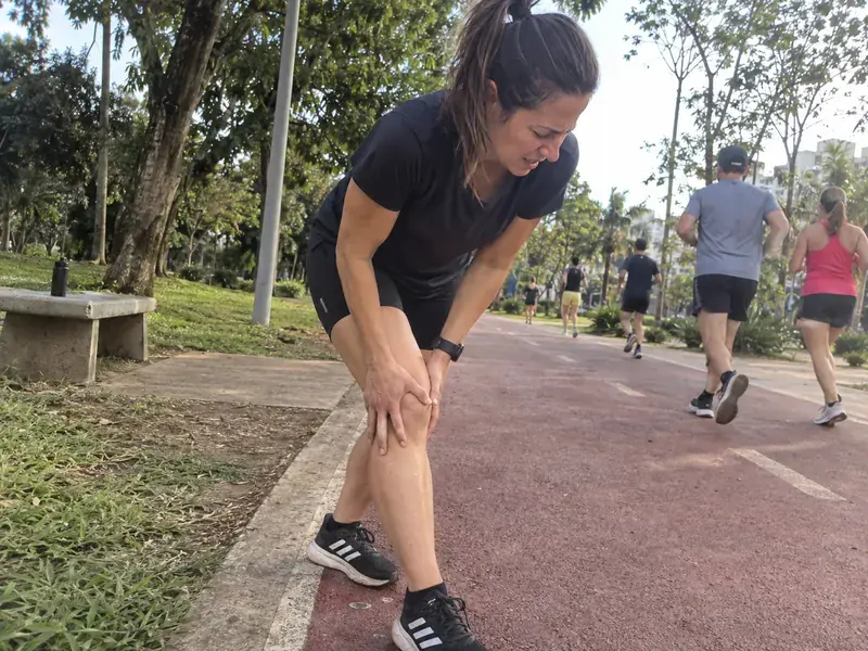 Corredora parada na pista do parque segurando o joelho depois de sentir uma lesão durante o treino
